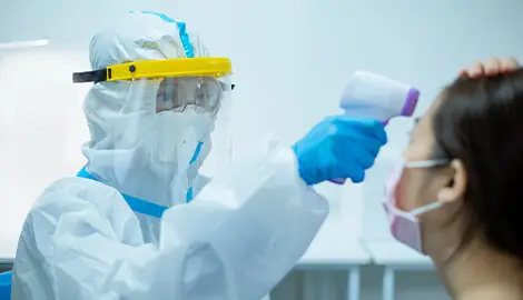 Worker in PPE checks patient’s temperature.