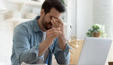 Stressed man rubbing eyes while working